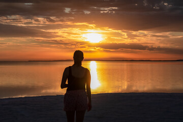 Fototapeta premium Silhouette of woman watching stunning sunrise of lake Bonneville Salt Flats, Wendover, Western Utah, USA, America. Dreamy red colored clouds mirroring on the water surface creating romantic atmosphere