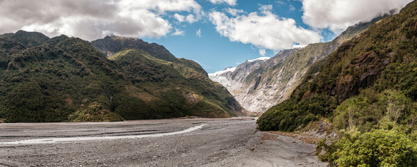 Panoramic view of the alluvial bed of the Waiho River flowing from the Franz Josef Glacier and snow capped mountains in New Zealand - Powered by Adobe