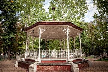 Bandstand in a city park in summer, surrounded by gardens and tall trees, with its typical round...