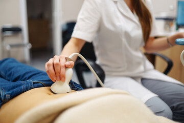 Obraz premium Doctor makes the patient women abdominal ultrasound. Ultrasound Scanner in the hands of a doctor. Diagnostics. Sonography. Pregnancy.