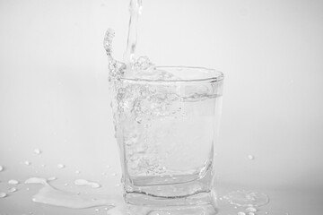 Pouring water into a glass causes splashes and water droplets on the floor.