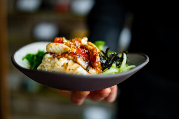 chef holding delicious donburi bowl with fish, rice and vegetables