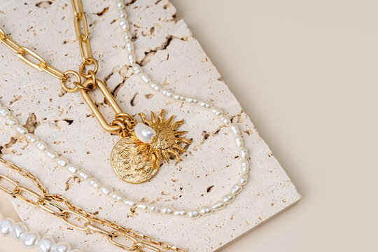 Trendy jewelry with chains, pearl necklace and pendant shapes moon and sun. Stylish golden bijouterie on the stone. Fashion accessories.