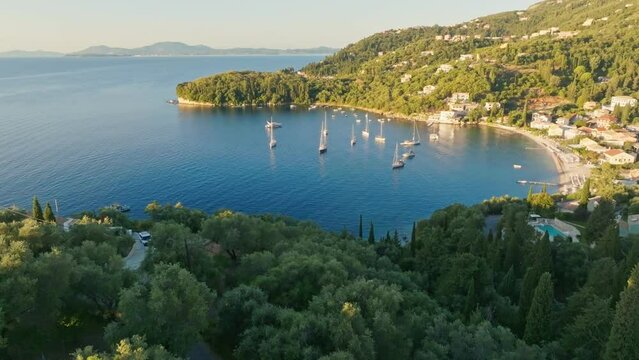 Flying over lush green vegetation, villas and sea bay with yacht on Corfu island. Gorgeous mediterranean landscape of Corfu island, Greece. Tourism landmark romantic honeymoon travel destination