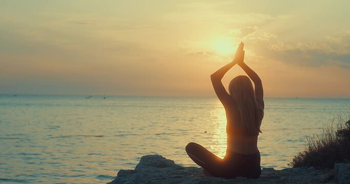 Women are doing yoga in summer sunset with sea background. Warm-up, healthy life, relaxing and outdoor exercise. Health care, authenticity, sense of balance and calmness.