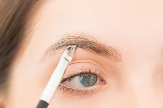 Young woman undergoing eyebrow correction procedure in beauty salon, closeup. Dying eyebrows whith brush