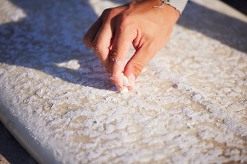 Hand, surfboard and wax with a sports man outdoor at the beach for surfing or recreation during...