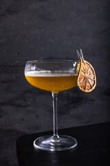Cocktail Angel Face fatto con apricot brandy, calvados e gin arte, guarnito con arancia essiccata fotografato su una superficie nera specchiata in un cocktail bar serale