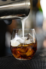 Barman mentre versa della panna fresca dallo shaker nel bicchiere del cocktail appena preparato in un cocktail bar 