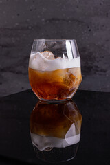 Cocktail White Russian con vodka, calua e panna fresca fotografato su una superficie nera a specchio