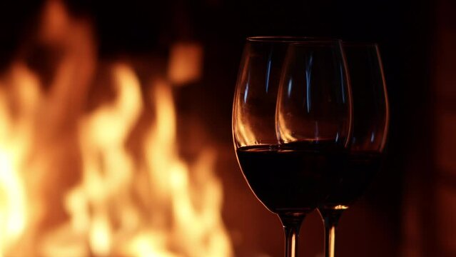 Two glasses of red wine on the background of fire in the fireplace. Holiday concept