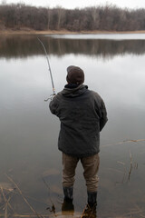 fisherman stands in water and catches fish with fishing rod....