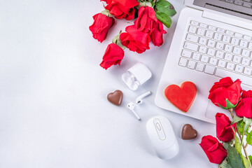Woman using her laptop with red roses. White laptop on white table background with chocolates, cookie hearts, red roses bouquet, flat lay working holiday, Valentine day background, top view copy space