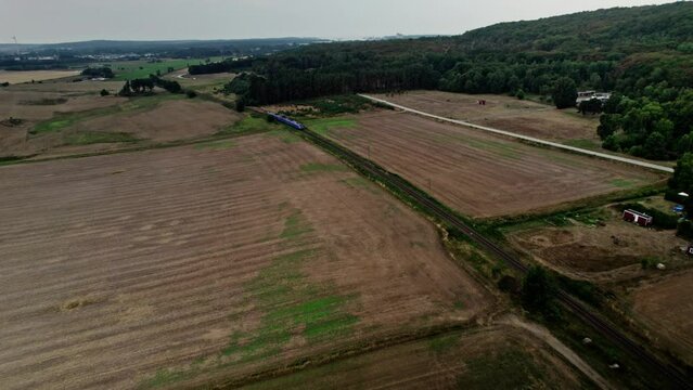 Aerial establishing shot,  an electrified passenger train on single track travel through the Swedish agricultural landscape in Solvesborg. Drone high angle view