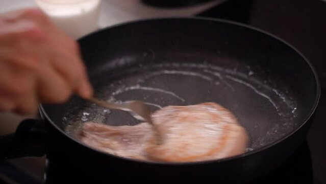Hands turn over meat steak, meat on bone in a frying pan, frying. 