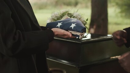 Cropped shot of unrecognizable military chaplain presenting US burial flag to widow of deceased veteran during outdoor funeral ceremony