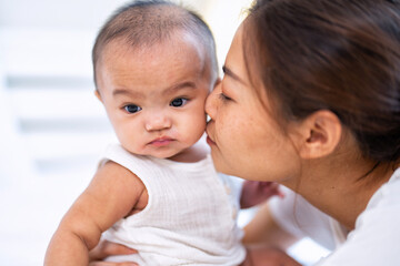 Mom happy joyful teasing asian infant baby new born sitting on bed and kiss her