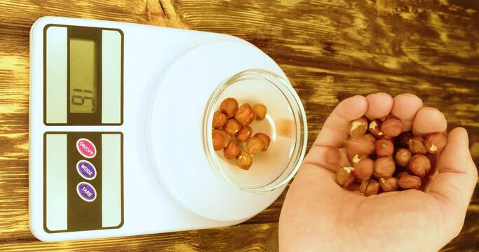 Male hand pours a portion of hazelnuts into a plate on a kitchen scale.