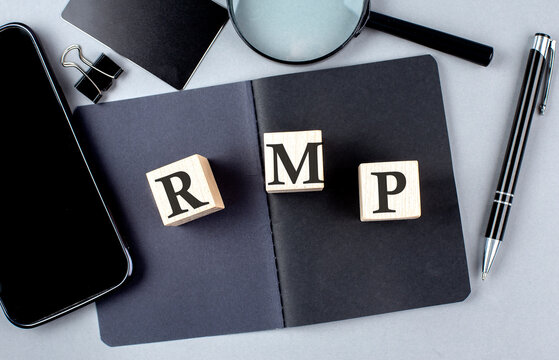 Word RMP on wooden block on black notebook with smartpone, credit card and magnifier