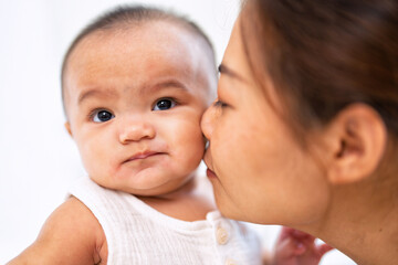 Mom happy joyful teasing asian infant baby new born sitting on bed and kiss her