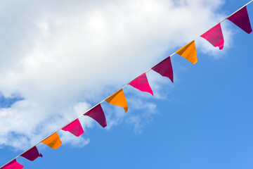 Pennants in pink, orange and purple hanging diagonal on a line against a blue sky and a white cloud, decoration for a festive summer event, copy space