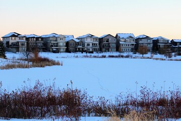 Fototapeta na wymiar A view of a beautiful lake, or retention pond, surrounded by reeds and homes in the winter evening in winter North Edmonton, in the neighbourhood of Crystalina Nera.