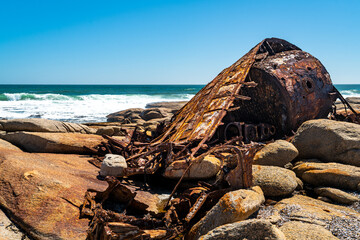 A rusty ship wreck lies on the rocks at the Atlantic Ocean Coast in South Africa.