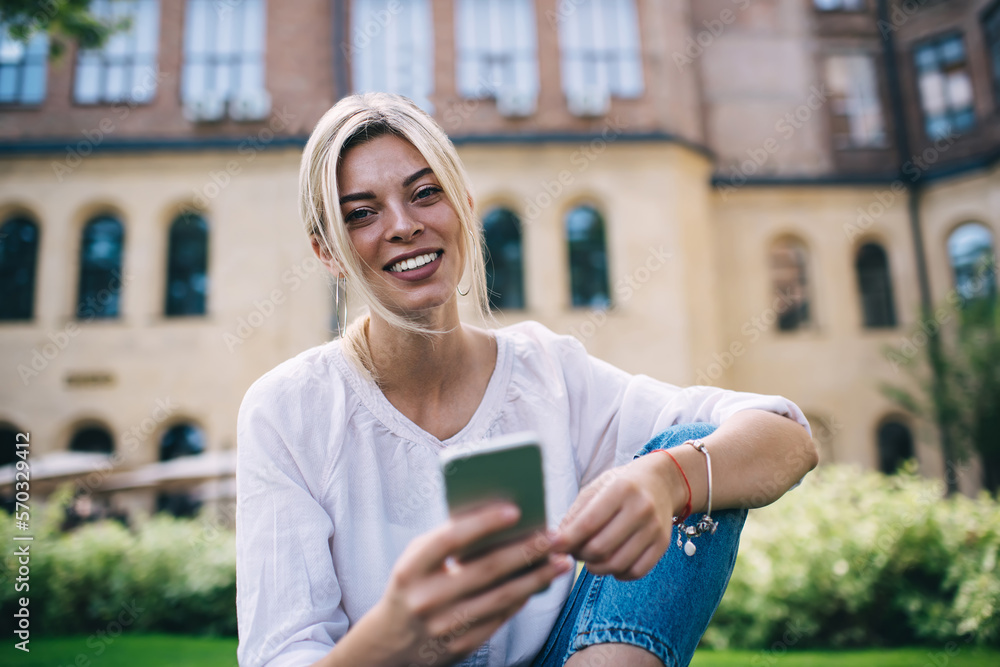 Poster portrait of cheerful travel blogger with modern cellular device smiling at camera during free time i