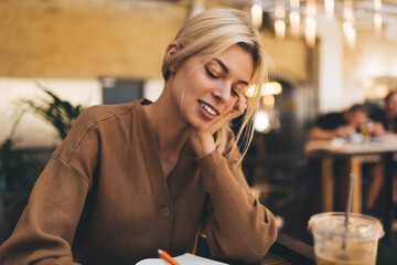 Happy Caucasian woman enjoying time for learning and education studying during free time in local coffee shop, young blonde female student with copped textbook planning organization indoors