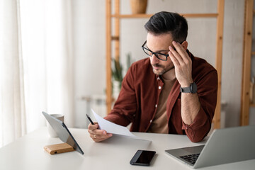 Contemplating businessman in home office concentrated on paperwork suffering from headache feeling...