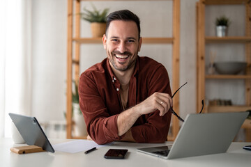 Smiling confident businessman looking at camera sitting at home office desk. Modern stylish...