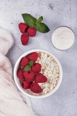Cottage cheese with fresh raspberries and sour cream on a light marble background.
