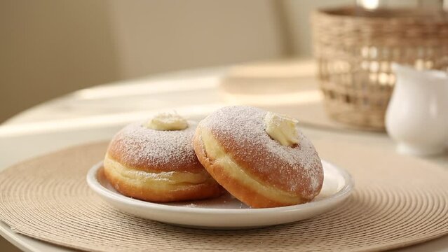 Preparing breakfast with Krapfen or berliner, or doughnut, or bombolone with cream filling. Shot motion of pouring hot tea.