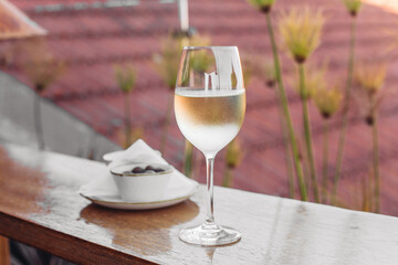 A glass of cold white wine, olives on a wooden table, city background 