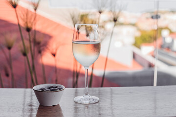 A glass of cold white wine, olives on a wooden table, city background 