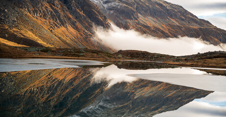 sunrise over the mountains sunset with fog and clouds over rocks and peaks in the swiss alps, julierpass lake like a mirror