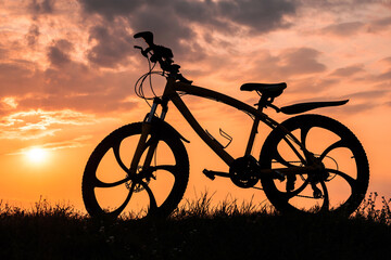 Fototapeta na wymiar Mountain bike silhouette against sunset sky with sun and clouds.