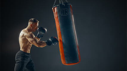 Boxer in action. Muscular shirtless male boxer exercising at punch bag