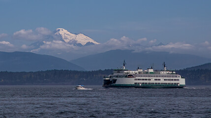 Fototapeta na wymiar A small powerboat and a Washington State Ferry transit the San Juan Islands near Anacortes, Washington with a stately Mount Baker towering in the background.