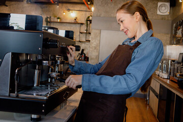 Portrait of a happy woman working in a coffee shop. Successful small business owner in casual brown apron making coffee. Cafe owner and small business concept