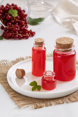 Homemade red currant syrup, juice or vinegar salad dressing in small glass bottles with fresh berries on white background. Selective focus, vertical.