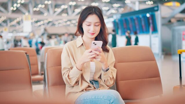 Asian tourist woman using mobile phone between waits for flight in Airport Terminal, Browse Internet, Post on Social Media, flight check check in, Tourist journey trip concept