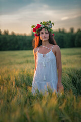 Portrait of a beautiful dark-haired girl with a wreath of flowers on her head on a summer field.