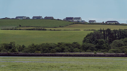 A houses on a hill, sky on a summer day. A small Irish village. The countryside in Ireland. Green grass field