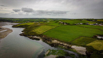 Obraz premium Green fields on the Irish hills, top view. The countryside of Ireland on a cloudy day. The coast of Clonakilty Bay at low tide. Green grass field under cloudy sky