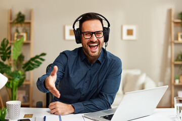 Handsome customer support man with a smile on his face is sitting at a desk and extending his hand for a handshake