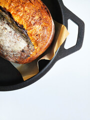 Sourdough bread in a cast iron pan right after baking. White background.