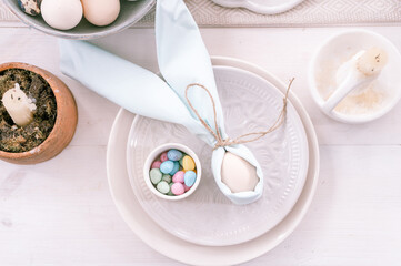 Fototapeta na wymiar happy easter holiday in springtime season. festive home decor. traditional food. white beige chicken egg wrapped in pale blue cloth like rabbit or bunny ears in plate and small candy eggs on table