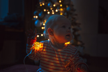 Cute little baby toddler near the Christmas tree playing with a garland and toys. The concept of the new year and Christmas mood