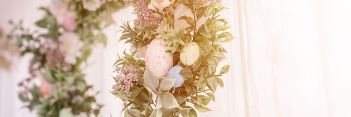 happy easter and spring holidays time. easter wreath with sprigs of lilac bush blossom flowers and leaves and decorated eggs on bright light window background. home interior decor. banner. flare